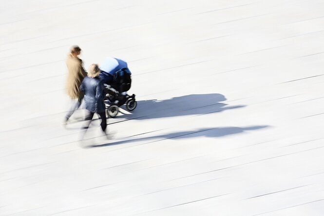 Zwei Menschen schieben einen Kinderwagen und unterhalten sich.