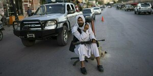 Ein bewaffneter Taliban in weisser Kleidung sitzt mit Waffe auf einem Bürostuhl auf der Straße