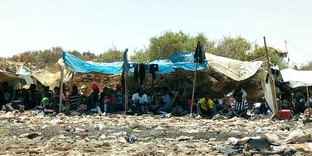Afrikanische Migranten sitzen unter einem selbstbebastelten Sonnenschutz in der Hitze