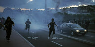 Vermummte Menschen rennen im Rauch bei einer Demonstration
