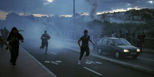 Vermummte Menschen rennen im Rauch bei einer Demonstration