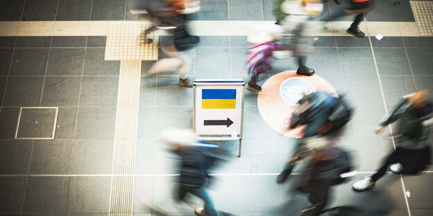 Ein Schild mit ukrainischer Flagge, drumherum laufende Menschen