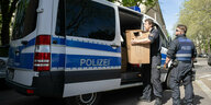 Polizisten holen Kartons aus einem Polizeikastenwagen