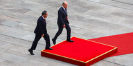 Der chinesische Premierminister und Olaf Scholz gehen auf ein mit rotem Teppich überzogenes Podest