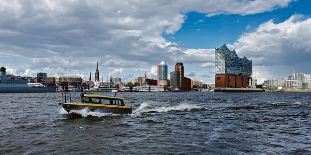 Ein Boot mit der Aufschrift "Elbtaxi" fährt über die Elbe. Im Hintergrund ist die Hamburger Stadtkulisse.