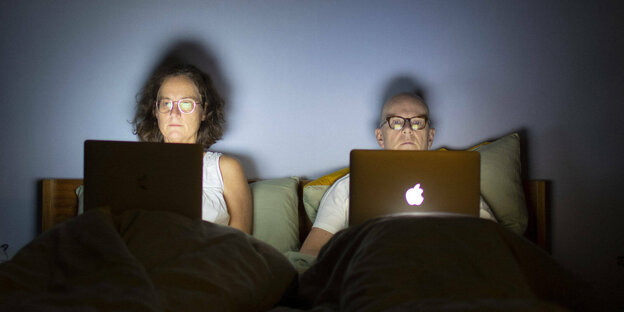 Ehepaar mit Notebooks im Bett.