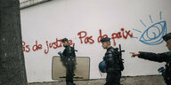 Polizisten vor einer Mauer, auf der geschrieben steht: "Pas de justice, Pax de paix"