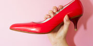 Eine Hand hält einen roten Schuh.