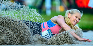 Vanessa Low landet in der Weitsprunggrube und der Sand spritzt um sie herum auf