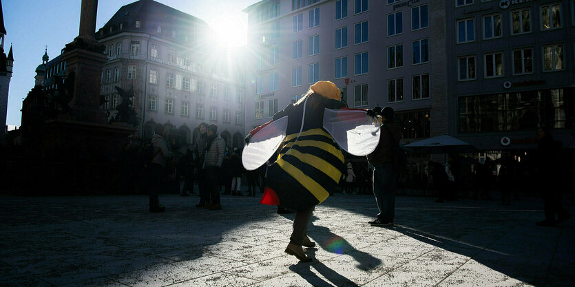 Eine als Biene verkleidete Person auf einem Platz im Gegenlicht