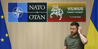 Selenski vor einer Wand mit den Emblemen der Nato und zwischen den Fahnen der EU un der Ukraine
