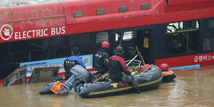 Ein Bus, umgeben von Wasser, davor ein Schlauchboot mit Rettungskräften