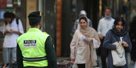 Ein Sittenpolizist steht auf der Straße. Zwei Frauen laufen in seine Richtung, eine mit, eine ohne Hijab