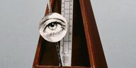 Ein Metronom, auf dessen Pendel das Bild eines Auges angebracht ist.