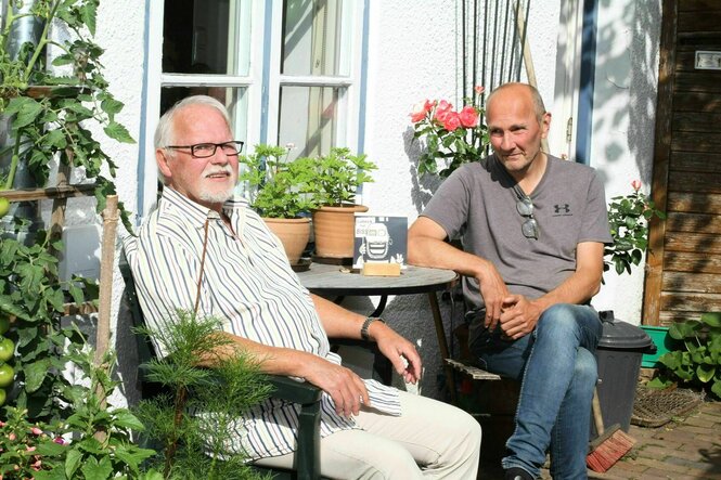 Rolf und Thomas sitzen auf einer sommerlichen Terrasse an einem kleinen Tisch