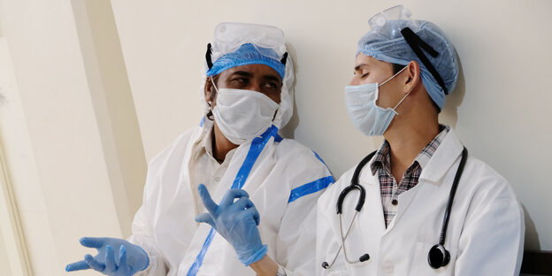 Zwei Menschen in medizinischer Schutzkleidung lehnen sich an eine Wand