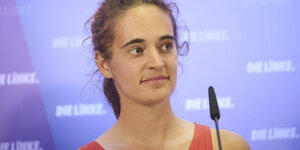 Carola Rackete vor einer blauen Wand mit Die Linke Logos