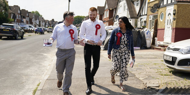 Jonathan Ashworth, Danny Beales, und Shabana Mahmood tragen Labour-Abzeichen und laufen eine Straße in einer Wohngegend entlang