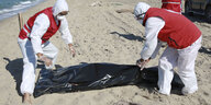 Libysche Rothalbmondmitarbeiter heben eine Leiche eines ertrunkenen Migranten am Strand in der Nähe der Stadt al-Chums auf.