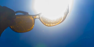 Eine Sonnenbrille wird gegen die Sonne vor blauem Himmel gehalten