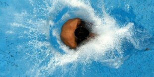 Ein Mensch trifft im Freibad klatschend auf's kalte Wasser.