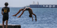 Ein Junge spring rückwärts ins Wasser, im Hintergrund die Krimbrücke