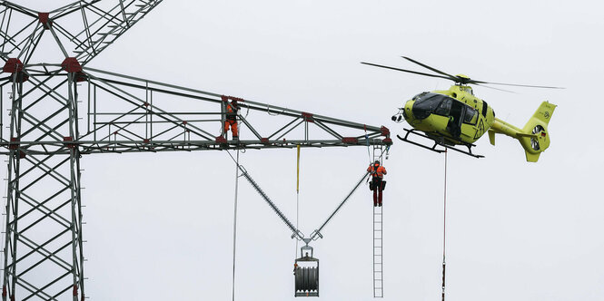 Gelber Hubschrauber bei der Montage zwischen Strommasten