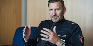 Ein Polizist sitzt gestikulierend und sprechend an einem Tisch