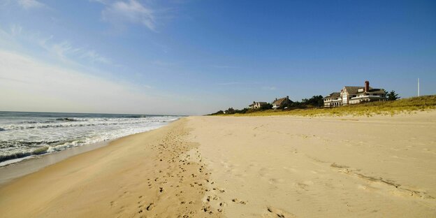 Fußspuren auf dem Strand am Meer, im Hintergrund Häuser auf dem Deich.