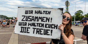 Ein weiblicher Rammmstein-Fan hält ein Schild in die Kamera. Darauf steht: "Wir halten zusammen" Wir halten euch die Treue!"