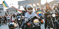 Demonstrationsteilnehmer:innen sitzen auf ihren Motorrädern. In der Hand schwingt eine Person eine Regenboggenflagge. Im Hintergrund ist das Brandenburger Tor zu erkennen.