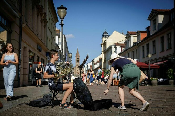 Eine Frau legt geld in den Instrumentenkasten eines Straßenmusikers