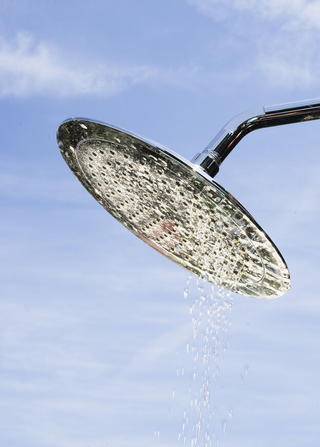 Wasser tröpfelt aus einem Duschkopf vor strahlenblauem Himmel