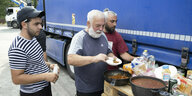 3 Männer nehmen gekochtes Essen von einer Pallette, dahinter ein LKW