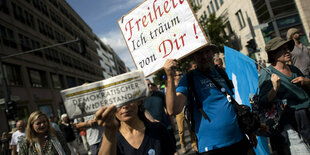 Protestierende mit Schildern, auf einem steht: "Freiheit, ich träum von dir", eine andere Person hält eine Ausgabe der Zeitung "Demokratischer Widerstand" in die Kamera