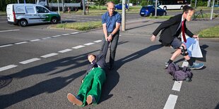 Dresden: Ein Mitglied der Protestgruppe Letzte Generation wird bei einer Sitzblockade an der Autobahnabfahrt am Elbepark von einem Autofahrer (M) beiseite gezogen. Die Demonstranten tragen Masken mit den Portraits von Bundeswirtschaftsminister Habeck und Bundeskanzler Scholz