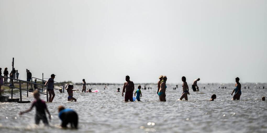 Menschen sind bei schönem Wetter am Strand von Harlesiel im Wasser.