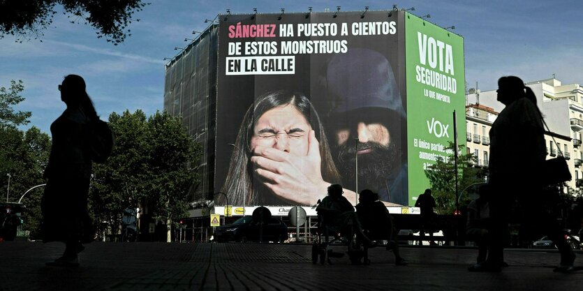 Fußgänger gehen in Madrid an einem riesigen Wahlplakat der rechtsextremen Partei VOX vorbei, auf dem zu lesen ist: Sanchez hat Hunderte dieser Monster auf die Straße gebracht