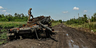 Ein zerstörter Panzer liegt am Rand einer schlammigen Piste. Auf ihm steht ein ukrainischer Soldat