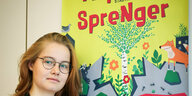 junge Frau lehnt an Plakat mit der Aufschrift Asphalt-Sprenger