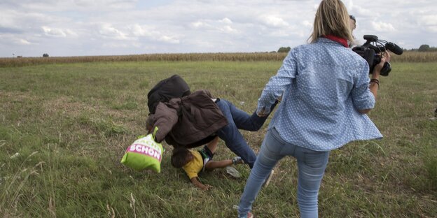 Ein Mann, der ein Kind trägt, fällt zu Boden, nachdem ihm eine Kamerafrau ein Bein gestellt hat