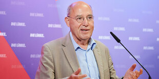 Gregor Gysi lächelnd am Mikrofon, an der Wand sind die Logos "Die Linke" angebracht