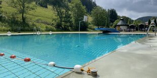 Freibad im Harzer Ort Wildemann, Besucher sind keine da. Links erheben sich Hügel. Der Himmel ist bedeckt.