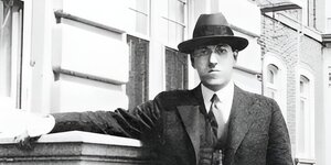 Ein Mann mit Hut und Anzug vor einem Haus