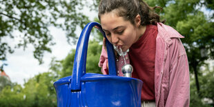 eine Frau beugt sich über einen Trinkbrunnen