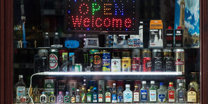 Eine Leuchttafel mit dem Schriftzug «Open Welcome» und zahlreiche alkoholische Getränke stehen in dem Fenster von einem Kiosk.