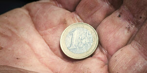Eine Euromünze auf einer dreckigen Hand.