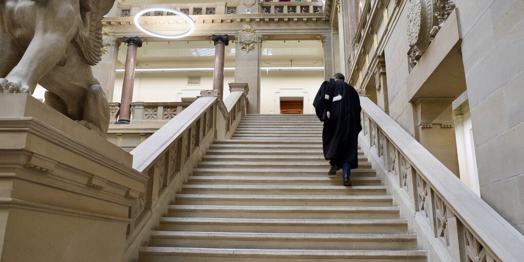 großer Treppenaufgang in einem alten Gebäude, ein Mann in Richterrobe geht hinauf