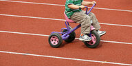 Kind mit Dreirad auf Laufbahn.