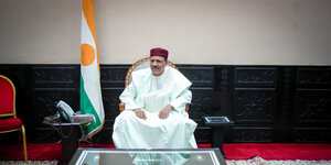 Staatspräsident Mohamed Bazoum sitzt in vor Nigers Flagge auf einem Stuhl.